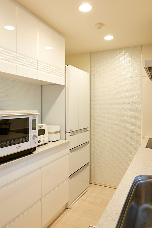 白でまとめられたキッチンスペースは、光沢のあるタイルの壁がアクセントに。