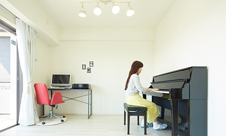 アップライトピアノやコンピュータは壁際に置いて、リビング・ダイニングのスペースをより広く使うようにしている。天井のスポットライトがピアノの場所を照らす。