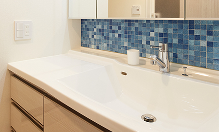 カウンターと洗面ボウルが一体形成された洗面室。三面鏡の下の壁面には青いタイルを貼ることで色のアクセントに。