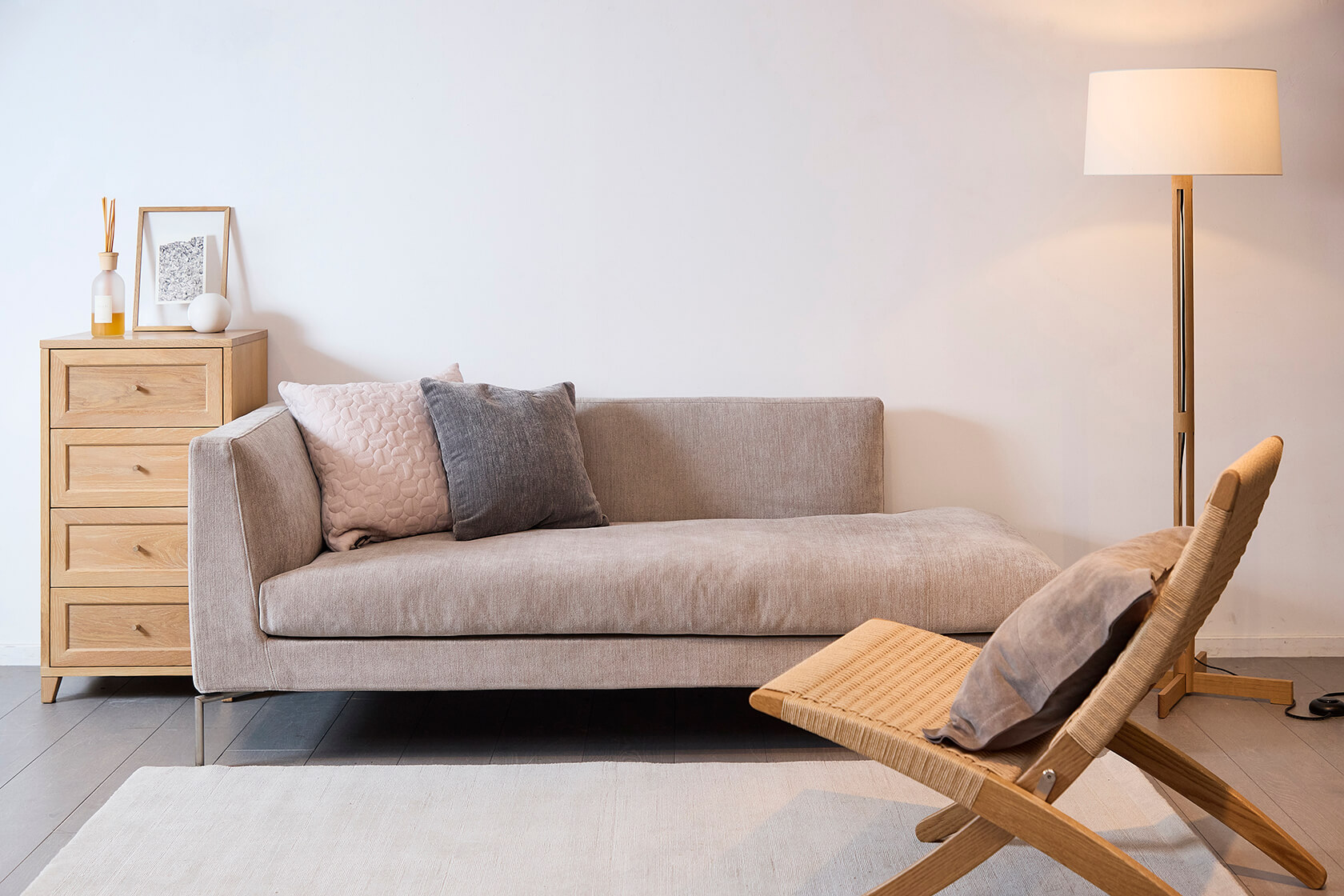 白壁にグレーの床、木製チェスト、ベージュの椅子、グレー系のソファやクッションなど、ベーシックカラーでナチュラルな雰囲気にまとめられています。