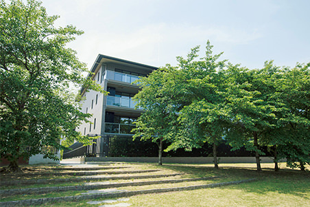 鴨川河畔、桜並木から見え隠れする５階建ての別館「AKATSUKI―暁―」の外観。２階以上のバルコニーはガラス製の手すりになっている。