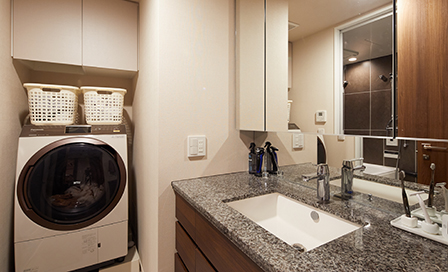 洗面室のカウンターはキッチンと同じ天然石。スタイリッシュな上に、汚れや水垢も一拭きで落ちるので掃除もラク。三面鏡の裏にはたっぷり収納スペースが。
