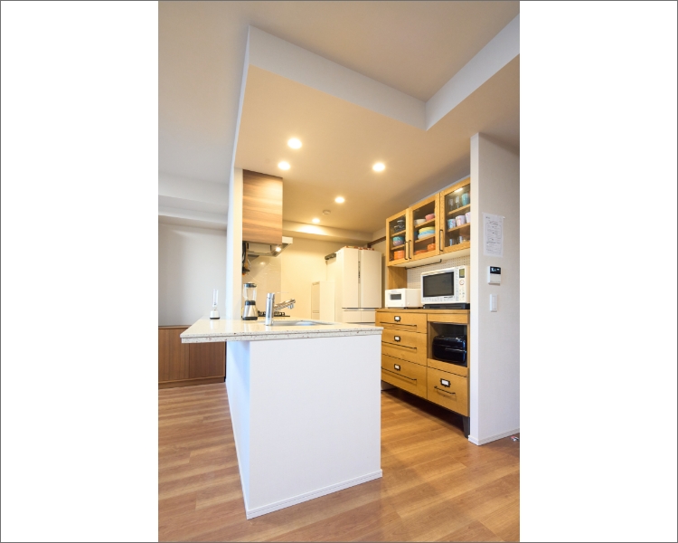 白い壁と天井に、木目調の床と家具がすっきりとした印象を与えるキッチンスペース。冷蔵庫、電子レンジ、オーブントースターなど、家電も白で揃えた。