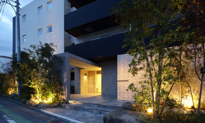 外壁意匠と照明計画を一新したエントランス。植栽の陰影が品格ある佇まいを印象づける。